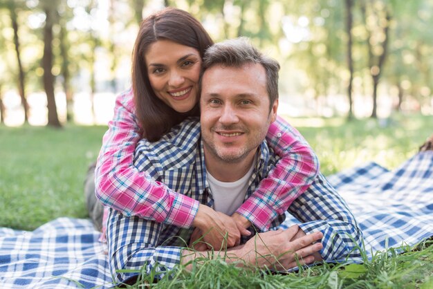 Happy romantic couple lying on blue blanket at park looking at camera