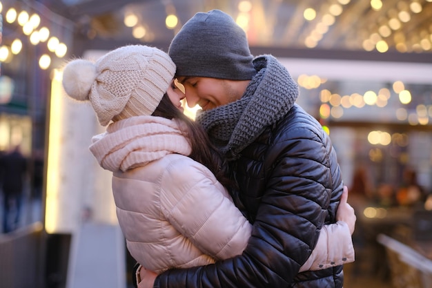 Free photo happy romantic couple wearing warm clothes hugging together in evening street near a cafe outside at christmas time