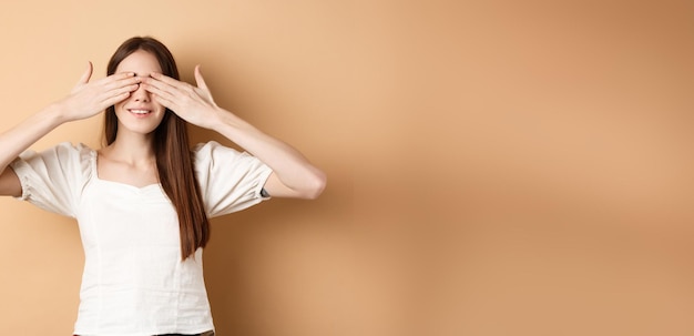 Happy romantic girl covering eyes and waiting for surprise smiling while anticipating gift standing