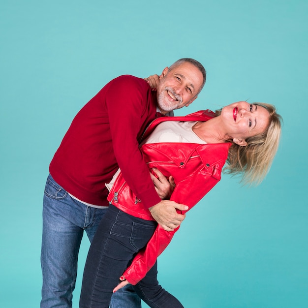 Happy romantic mature couple standing against turquoise background