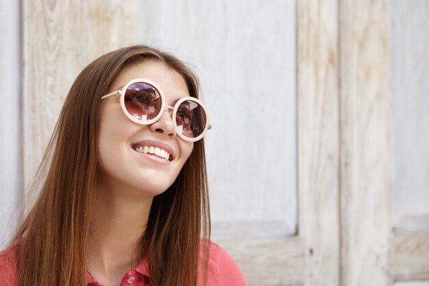 Happy romantic young woman in stylish round sunglasses with mirror lenses looking up with inspired joyful smile.