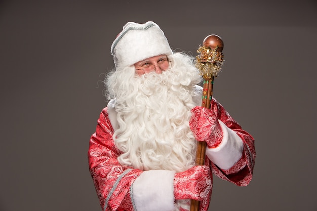 Happy Santa Claus in eyeglasses with staff looking at camera on black background