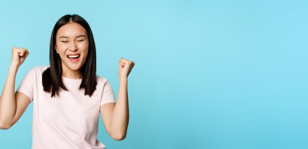 Free photo happy satisfied korean girl winning celebrating victory triumphing with fist pump scream of joy stan