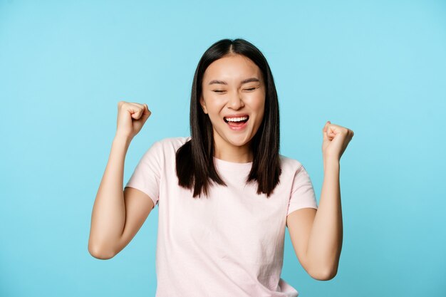 Happy satisfied korean girl winning celebrating victory triumphing with fist pump scream of joy stan...