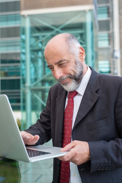 Happy satisfied mature businessman with laptop watching content