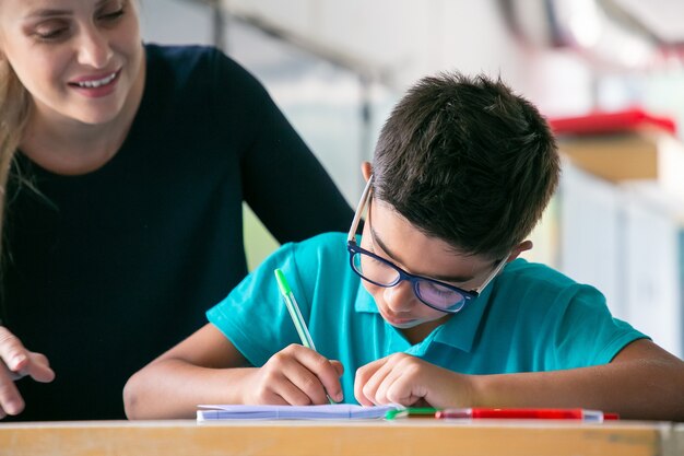 眼鏡をかけた男子生徒がクラスで仕事をしているのを見て幸せな学校の先生