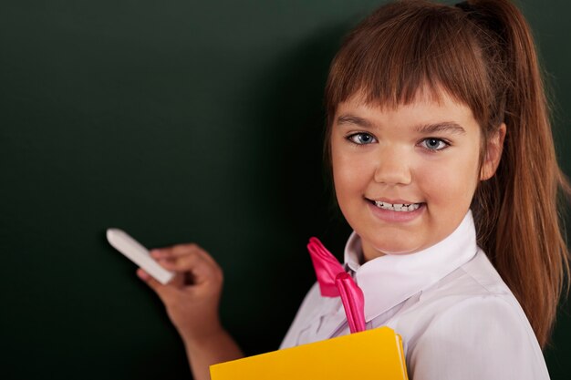 Happy schoolgirl writing on blackboard