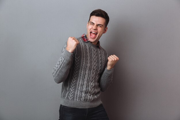 Happy screaming brunette man in sweater rejoice and looking away