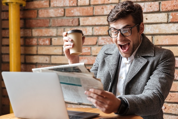 Happy screaming businessman in eyeglasses sitting by the table