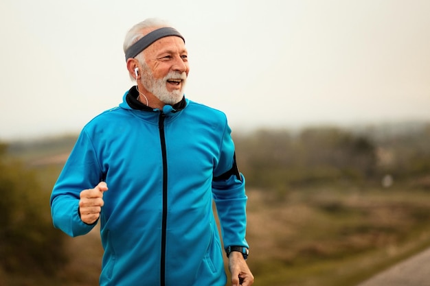 Happy senior athlete listening music on earphones while running in nature Copy space