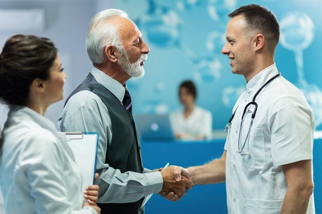 Happy senior businessman and male doctor handshaking while greeting in a hallway at clinic