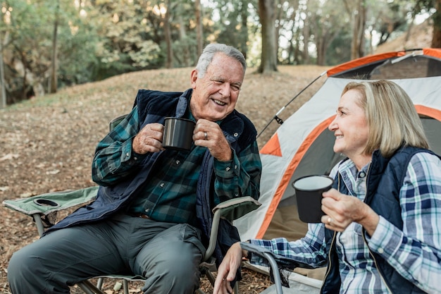 森のテントのそばでコーヒーを飲む幸せな年配のカップル