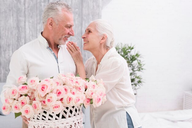 Happy senior couple looking at each other holding basket of roses in hand