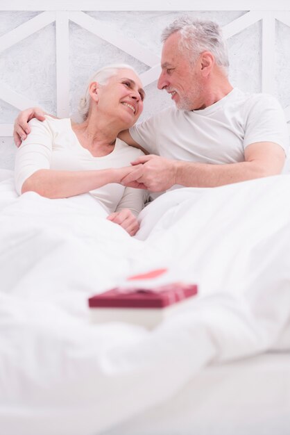 Happy senior couple lying on bed with gift box