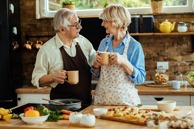 Happy senior couple preparing food and communicating while having a cup of coffee in the kitchen