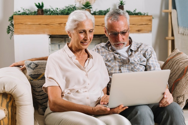 Happy senior couple sitting on sofa looking at laptop