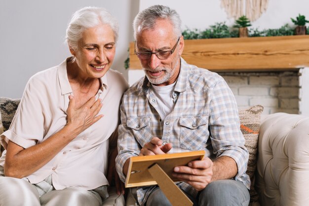 Happy senior couple sitting on sofa looking at picture frame