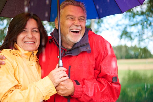 雨の間に立っている幸せな年配のカップル