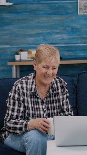 Happy senior couple waving at videocall with nephews using laptop