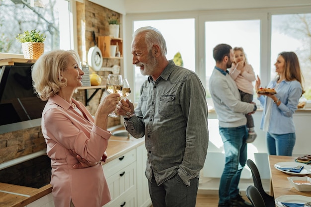 Счастливые пожилые муж и жена пьют вино перед семейным обедом на кухне
