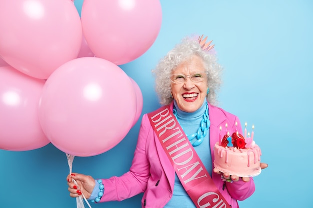 La signora anziana felice sorride ampiamente mostra i denti bianchi che festeggiano il compleanno