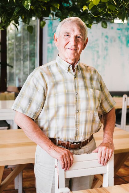 Happy senior male standing in cafe leaning on chair