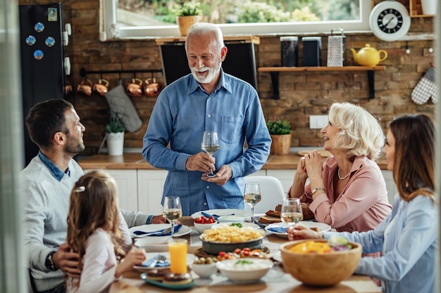 Happy senior man holding a toast while having lunch with his family at dining table.