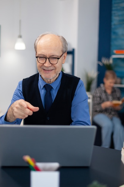 Happy senior man pointing at laptop during video conference