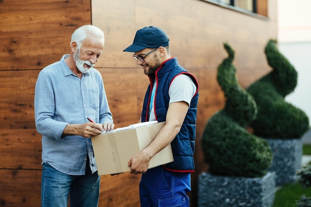 Happy senior man receiving packages and signing to postman for a home delivery