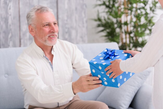 Happy senior man sitting on sofa receiving gift front a boy