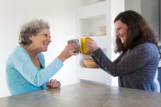 Happy senior mother and adult daughter toasting tea