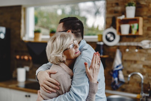 Happy senior mother and her adult son embracing in the kitchen