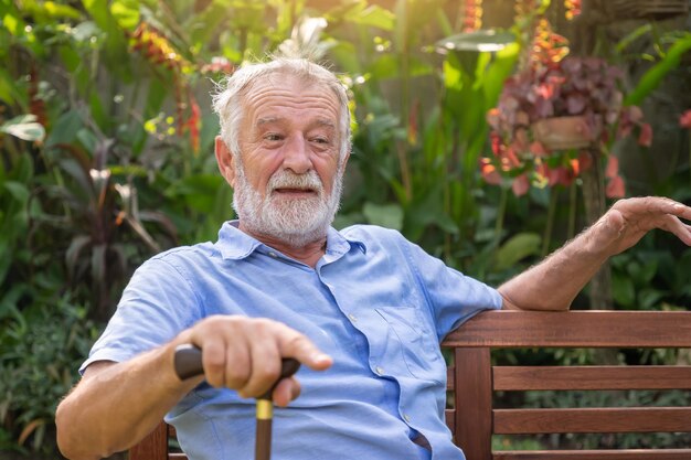 Счастливый пожилой кавказец с тростью сидит на скамейке в саду