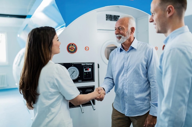 Happy senior patient and female doctor shaking hands after hyperbaric oxygen therapy at clinic