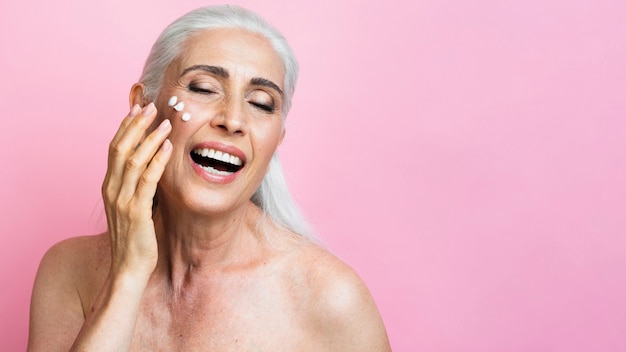 Happy senior woman applying moisturizer