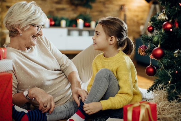 Happy senior woman and her granddaughter talking while relaxing at home on Christmas