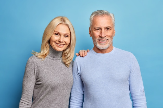 happy senior woman and man express positive emotions pose together being still in love isolated over blue wall