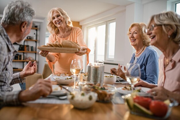 家で昼食時に友達にパンを提供する幸せな年配の女性