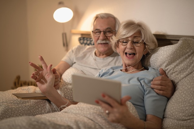 Happy senior woman singing while listening music on digital tablet with her husband in bedroom