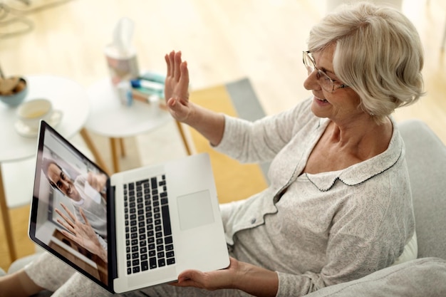 Free photo happy senior woman waving while having video call with her son from home