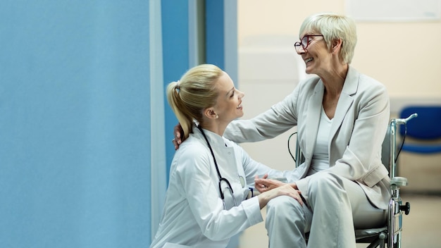 Happy senior woman in wheelchair communicating with a nurse in a hallway at clinic