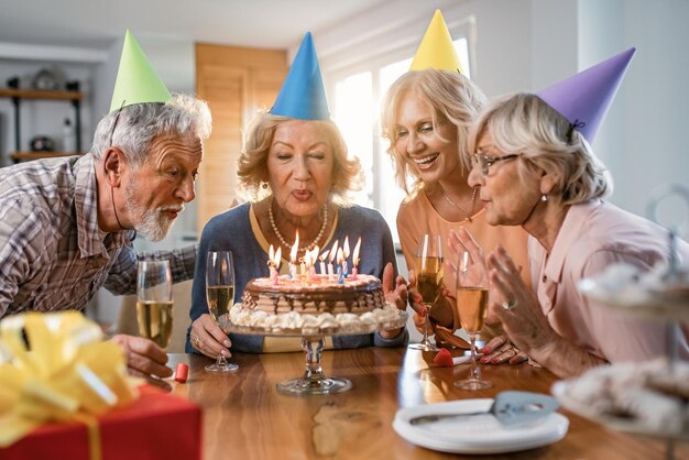 집에서 생일 파티를 하는 동안 케이크에 촛불을 불면서 즐거운 시간을 보내는 행복한 노인들