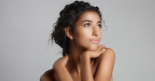 Happy serene young woman with beautiful olive skin and curly hair ideal skin and brown eyes in studio