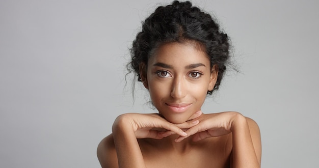 Happy serene young woman with beautiful olive skin and curly hair ideal skin and brown eyes in studio