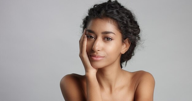 Happy serene young woman with beautiful olive skin and curly hair ideal skin and brown eyes in studio