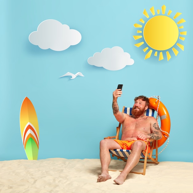 Foto gratuita felice torso nudo barbuto uomo rosso in posa sulla spiaggia