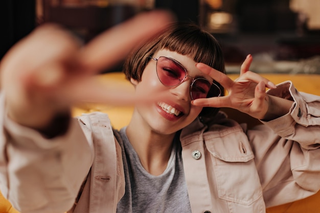 Free photo happy short haired woman in light clothes smiling and sitting on yellow couch in cafe