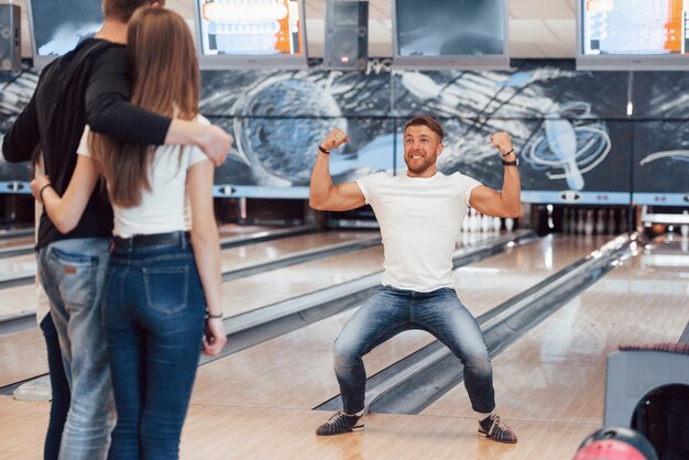 Happy and showing muscles. Young cheerful friends have fun in bowling club at their weekends