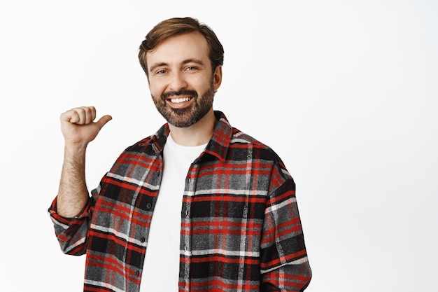 오른쪽을 가리키며 웃으면서 흰색 배경 위에 체크 셔츠를 입은 광고를 보여주는 행복한 단순한 남자