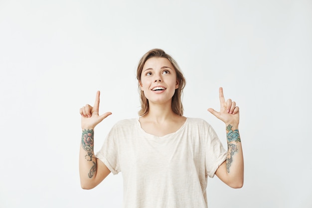 Happy sincere young girl pointing fingers up smiling .